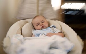 Baby sleeping in a swing with a baby monitor nearby