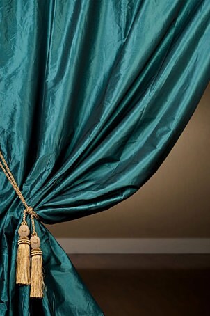 Teal curtains are held back with gold tassles