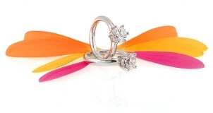 Two diamond engagement rings and a handful of colorful flower petals form a butterfly