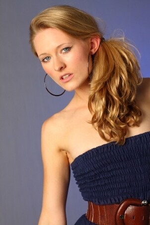 Beautiful blond model wearing a blue dress, a brown belt and large silver hoop earrings