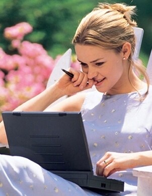 Pretty woman sits outdoors working on her laptop and wearing a blue dress and diamond earring studs