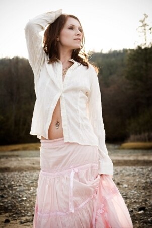 Lovely bohemian girl wearing a sparkling body jewelry belly ring, a long pink skirt and a white shirt