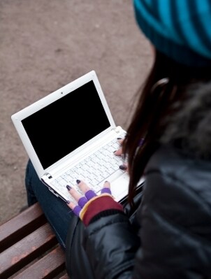 Girl on a bench typing on a netbook