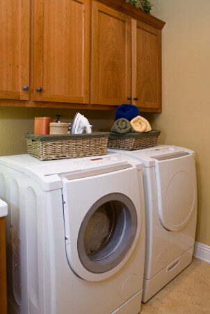 Modern laundry room with white side-by-side washer and dryer, baskets with supplies and custom cabinets