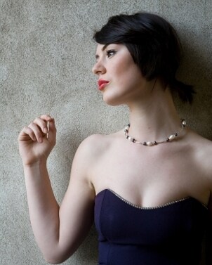 A gorgeous woman with porcelain skin and velvety rose lips wearing a blue cocktail dress and a trendy pearl necklace