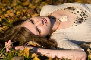 A pretty girl with auburn hair lying in a field and wearing a sweater and a floral pendant