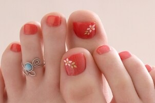 A woman with a bright orange floral pedicure wearing a turquoise and silver toe ring