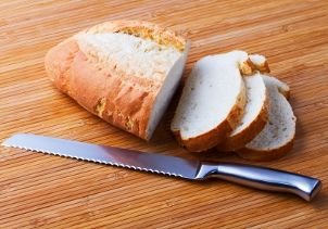Serrated knife lays next to sliced French bread loaf